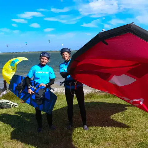 Élèves avec leurs planches et un kite sur l'herbe en bord de lac