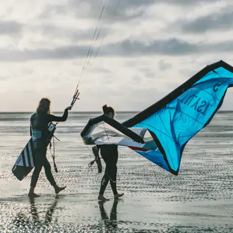 Deux kitesurfeurs avec leur aile sur le sable mouillé