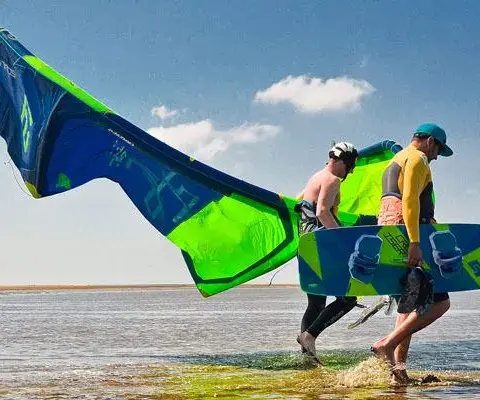 Deux kitesurfeurs portant kite et planche dans l'eau peu profonde