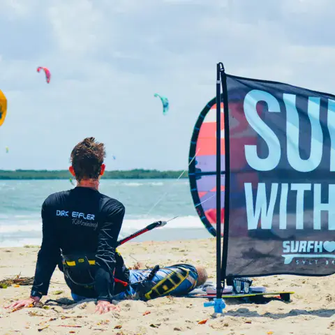 Kitesurfeur assis sur la plage près d'un drapeau de l'école