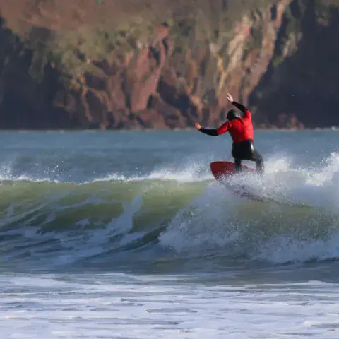 Surfeur sur une vague devant une falaise