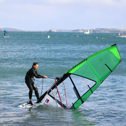 Windsurfeur debout sur sa planche dans la baie