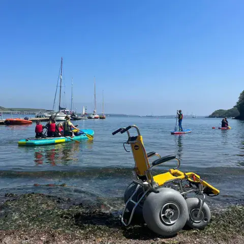 Fauteuil de plage adapté, paddle et voiliers dans la baie