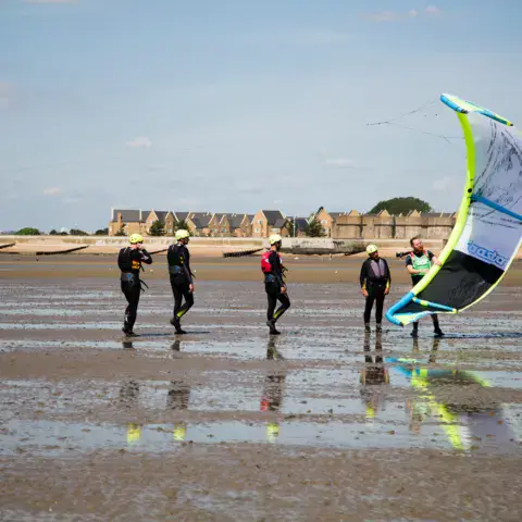 Élèves en combinaison avec un kite sur la plage