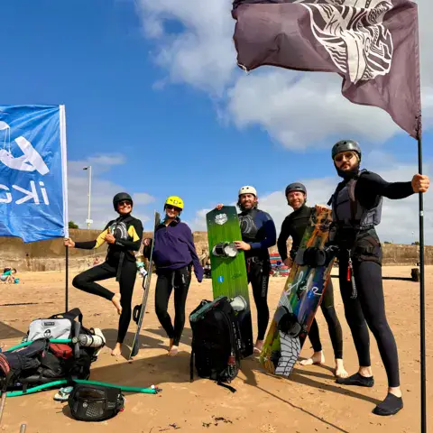 L'équipe et des élèves sur la plage avec drapeaux et planches