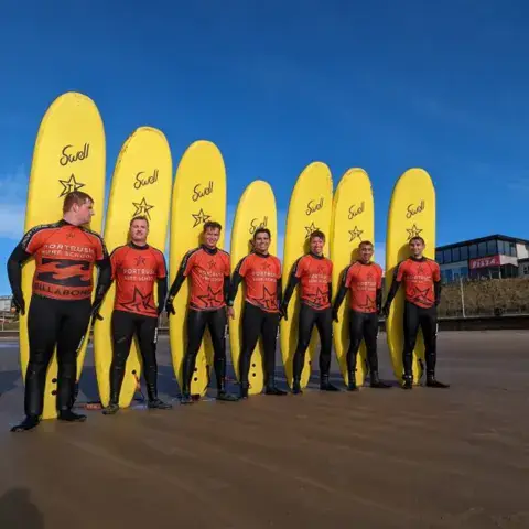 Équipe de moniteurs alignée devant des planches jaunes sur la plage