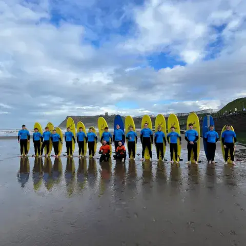 Rangée d'élèves avec leurs planches jaunes sur la plage