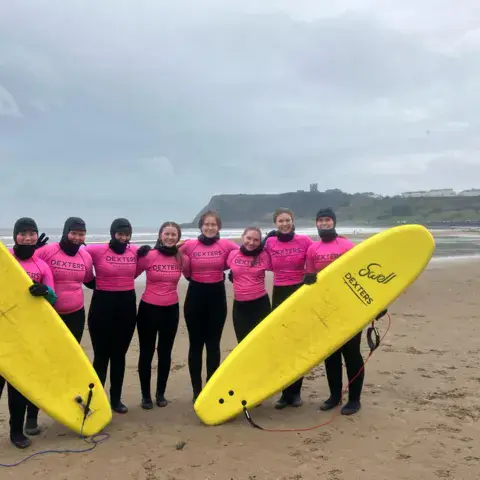 Groupe avec des planches de surf jaunes, le château de Scarborough en fond