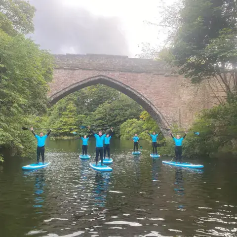 Groupe de paddleurs bras levés sous un pont de pierre