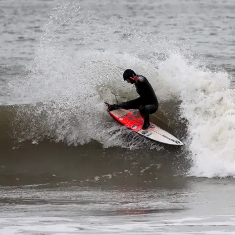 Surfeur en pleine manœuvre sur une planche rouge et blanche