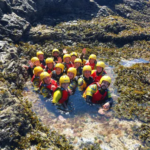 Groupe de coasteering casqué dans une mare entre les rochers