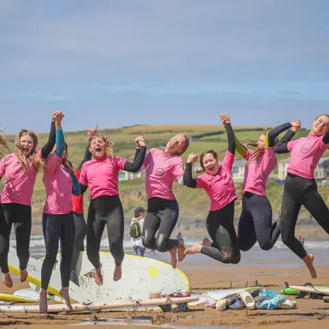 Groupe de surfeurs en combinaisons roses qui sautent sur la plage