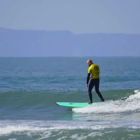 Moniteur en maillot jaune qui surfe une petite vague sur une planche verte