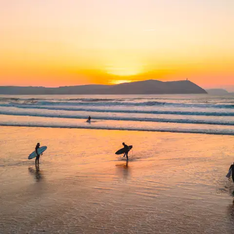 Surfeurs sur la plage au coucher du soleil, face à la baie
