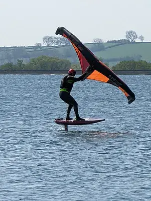 Wingfoiler sur plan d'eau calme, aile orange tenue à bout de bras