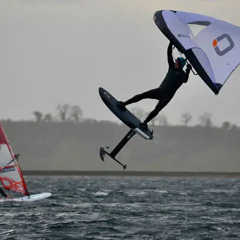 Wingfoiler en saut et windsurfeur au second plan sur le plan d'eau