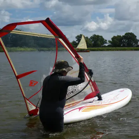 Windsurfeur relevant sa voile dans l'eau peu profonde