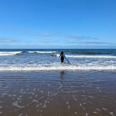 Un surfeur entre dans l'eau, planche sous le bras
