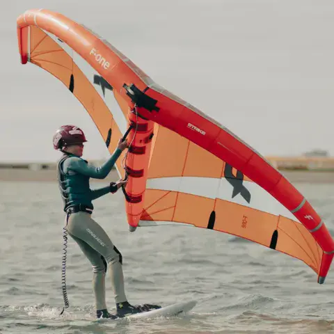 Rider debout sur une planche avec une aile orange de wing foil