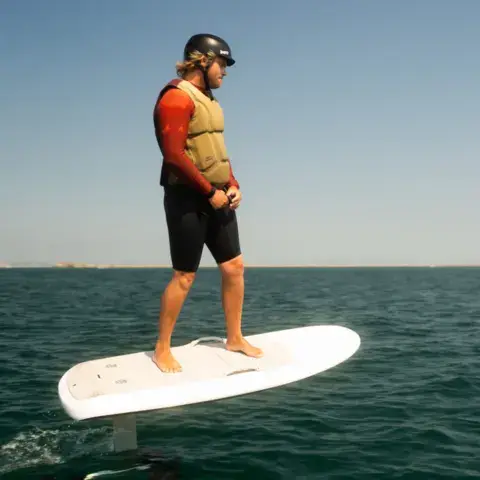 Pilote debout sur une planche à foil électrique, casqué et gilet