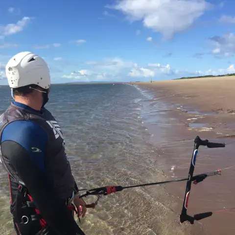 Kitesurfeur casqué dans l'eau peu profonde, barre en main