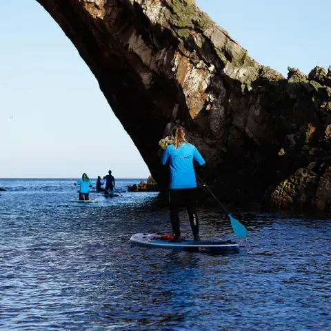 Sortie en stand up paddle sous une arche rocheuse de la côte