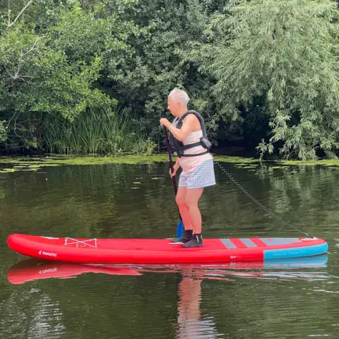 Pagayeuse debout sur un paddle rouge, au bord des roseaux