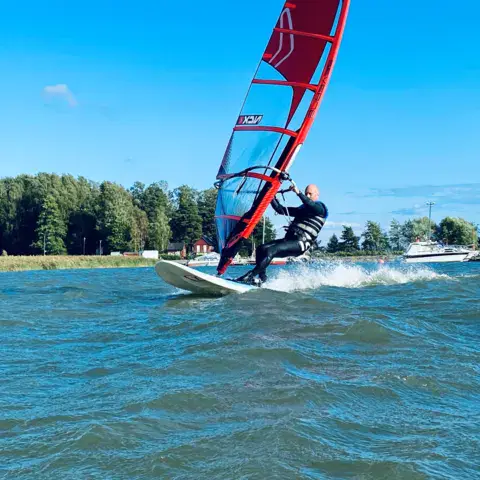 Planchiste filant sur l'eau le long d'une rive boisée
