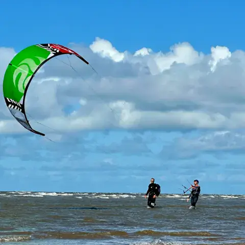 Deux kitesurfeurs sous une aile verte, en eau peu profonde