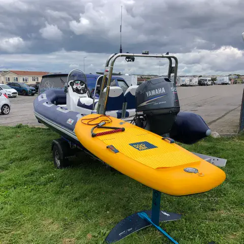 Une planche à foil posée devant un bateau pneumatique de sécurité