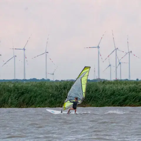 Un véliplanchiste sur le lac, avec des éoliennes à l'horizon