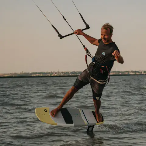 Un kitesurfeur sur une planche avec foil, au coucher du soleil