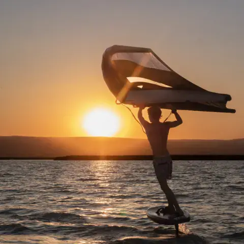 Une aile de wing au-dessus d'un foil, à contre-jour sur le lac