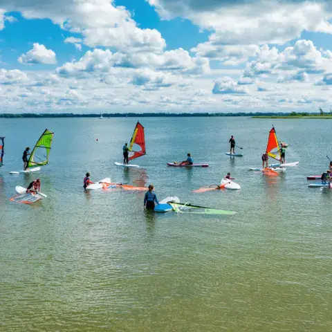 Groupe de windsurf en cours sur l'eau peu profonde du lac