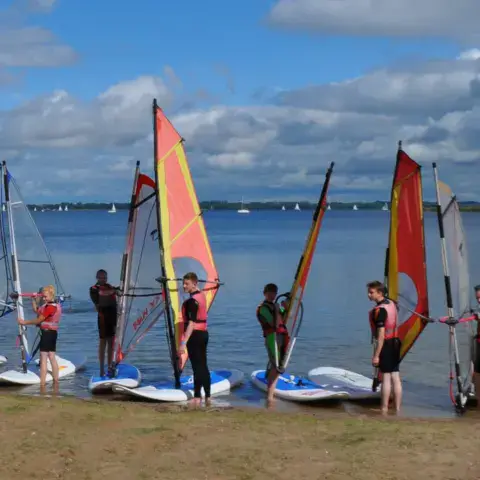Planches et voiles de windsurf alignées au bord de l'eau