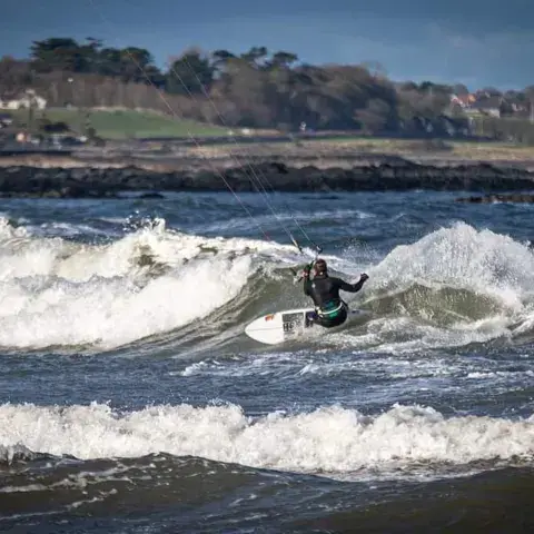 Un kitesurfeur sous son aile, avec la côte en arrière-plan
