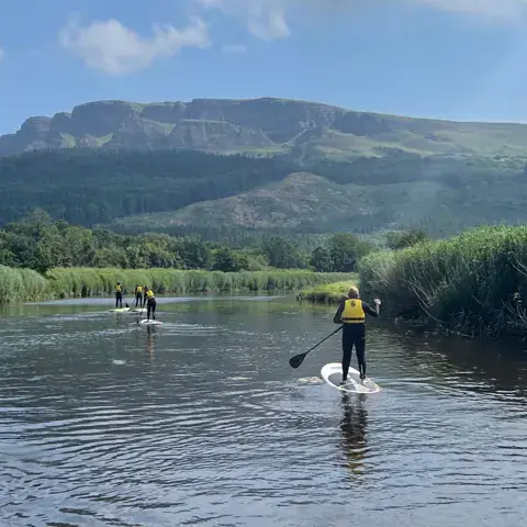 Sortie de stand up paddle sur une rivière, avec des montagnes en fond