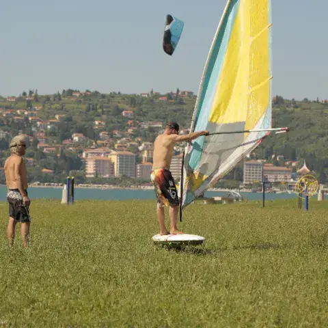 Une planche à voile gréée sur l'herbe, avec la ville côtière en arrière-plan