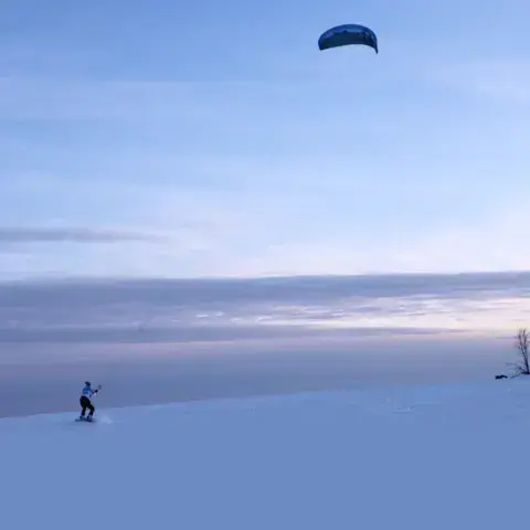 Un snowkiteur sur une pente enneigée, avec son aile dans le ciel
