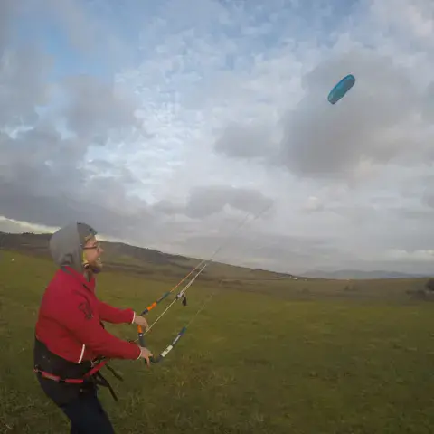 Un kiteur sur terre dans la campagne, avec son aile haut dans le ciel