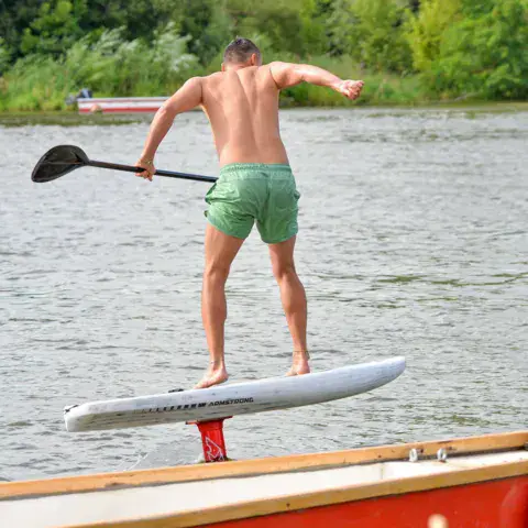 Un pratiquant debout sur une planche de paddle à foil, une pagaie à la main