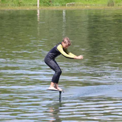 Une pratiquante de foil en équilibre sur sa planche, au-dessus de l'eau