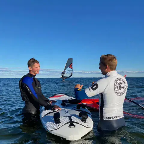 Moniteur donnant des conseils à un élève sur une planche de windsurf