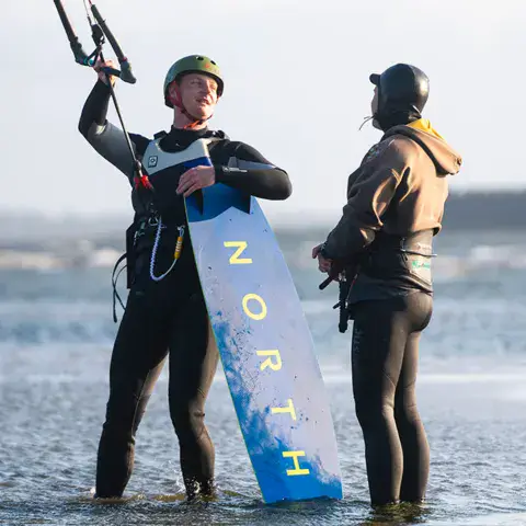 Deux kitesurfeurs échangeant au bord de l'eau avant la session