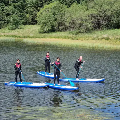 Un groupe en stand up paddle sur un lac entouré de bois