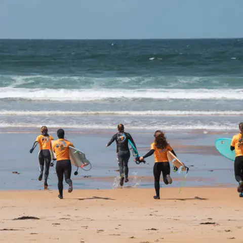 Élèves en combinaison qui courent vers l'eau avec leur planche