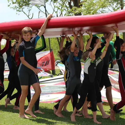 Groupe portant une grande planche de paddle sur la pelouse
