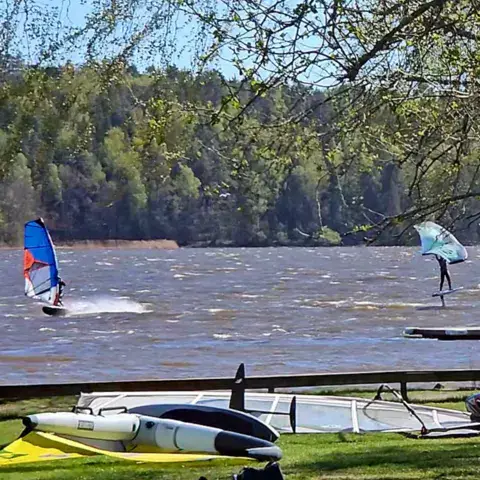 Windsurfeurs sur le lac, matériel posé sur la pelouse