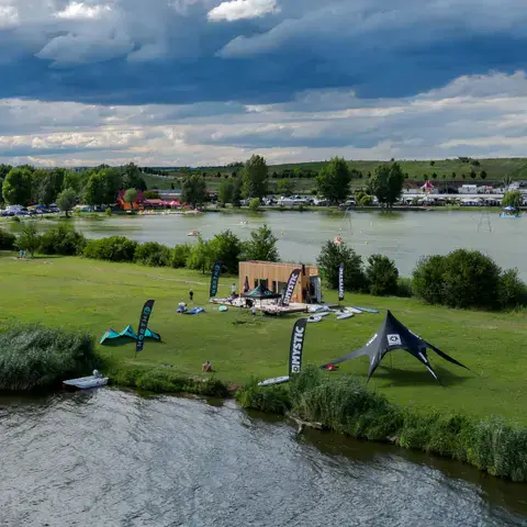 Vue aérienne d'un site herbeux au bord de l'eau, avec des kites posés au sol