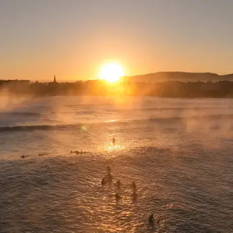 Surfeurs dans l'eau face au soleil levant